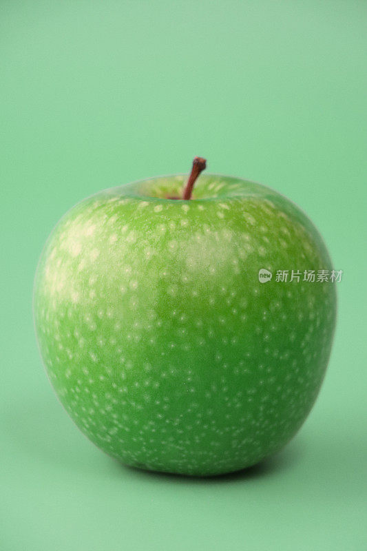 个体的特写图像，绿色的史密斯苹果(Malus domestica)，有茎，光滑，有斑点的果皮，浅绿色背景，重点在前景